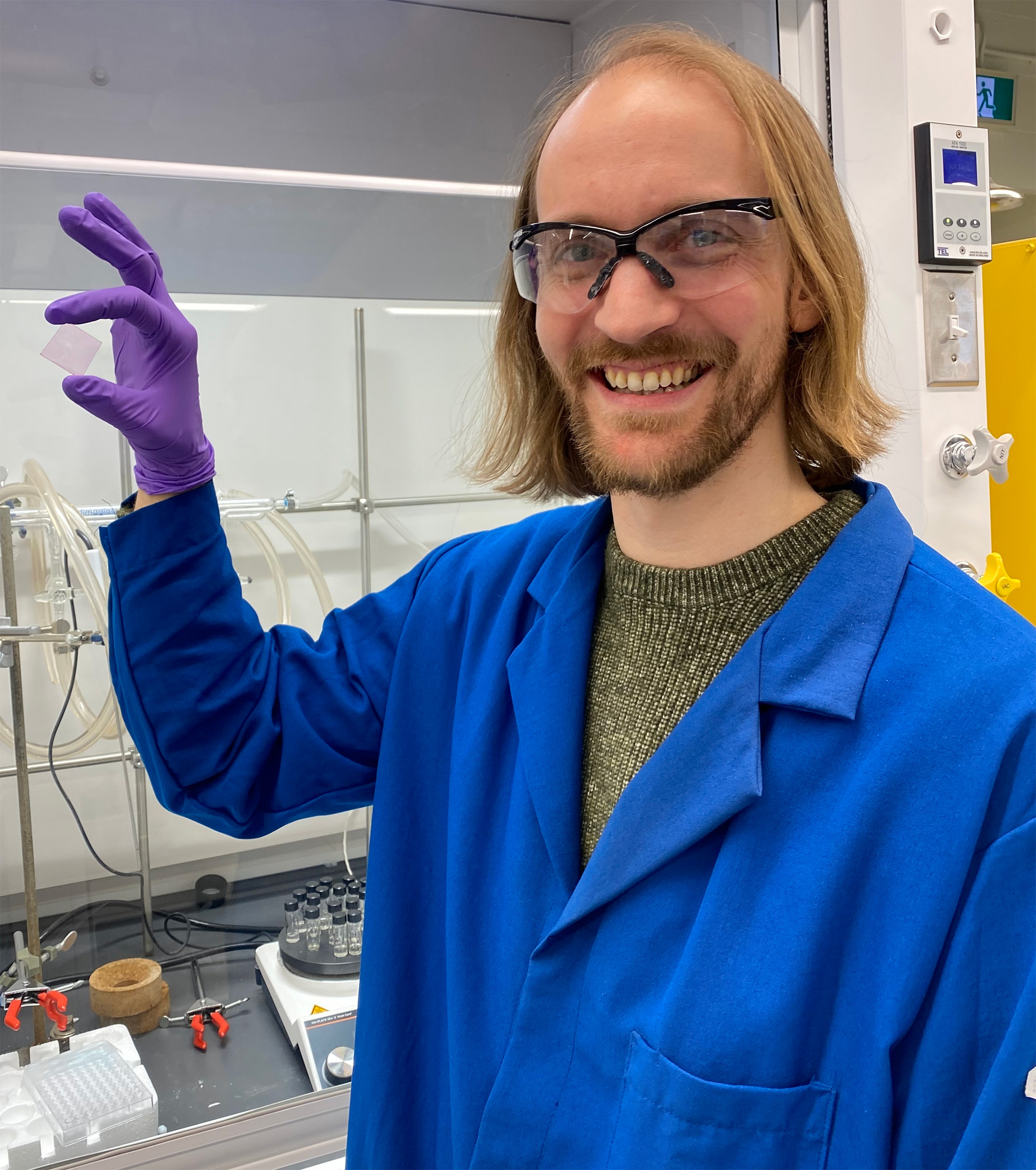 Bryton Varju poses in PPE, holding up a small square object.