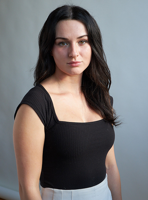 Portrait shot of a white woman with long, brown hair and a dark tank top looking into the camera.