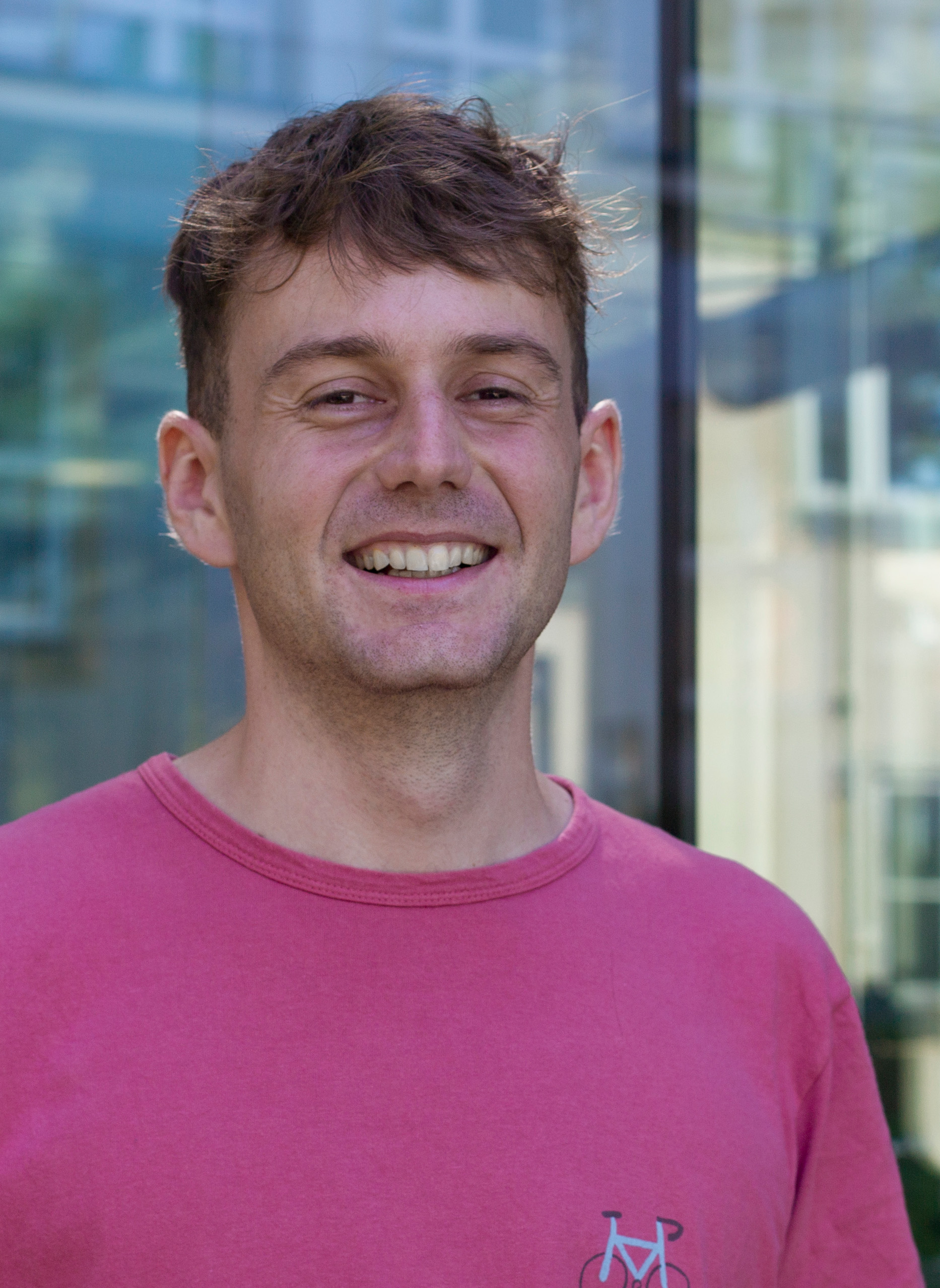 Closeup of a white man in a pink shirt smiling into the camera.