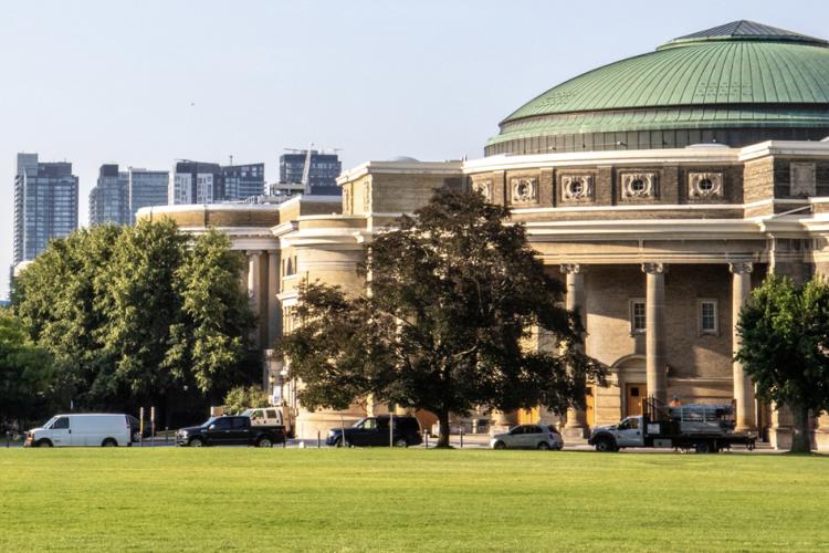 A building with a dome sitting behind a lawn and screen of trees.