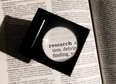 A magnifying glass sitting on a dictionary page, illuminating the word research