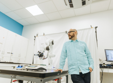Photo of Prof. Alán Aspuru-Guzik posing with a robotic arm in The Matter Lab 