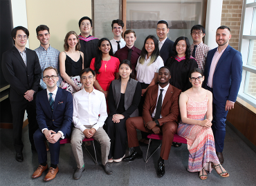 A group of 17 well-dressed adults clusters together, smiling at the camera.