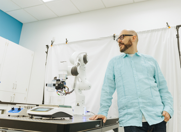 Photo of Prof. Alán Aspuru-Guzik posing with a robotic arm in The Matter Lab 