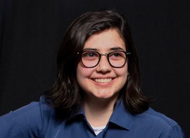 Head shot of a smiling white woman with glasses and shoulder-length dark hair.